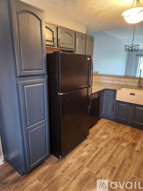 A black refrigerator in a kitchen with wooden flooring.