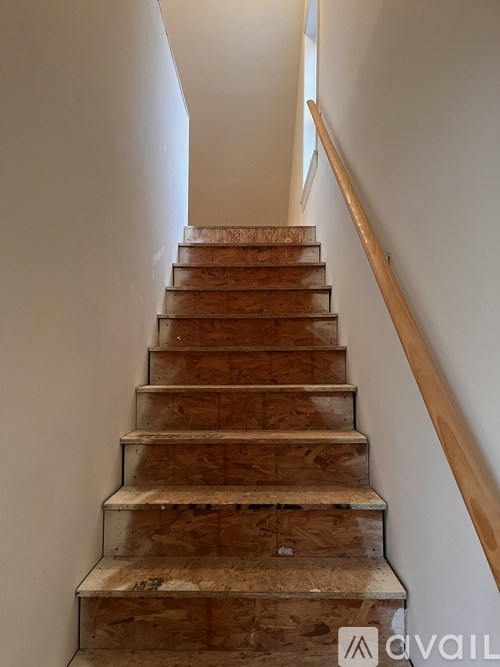 A wooden staircase with a white wall on one side and a wooden handrail on the other.