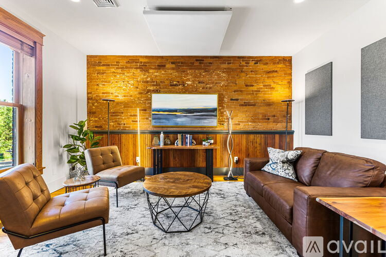 A living room with a brown leather sofa, a wooden coffee table, and a brick wall.