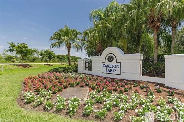 A sign that says "Carlton Lakes" is surrounded by flowers and palm trees.