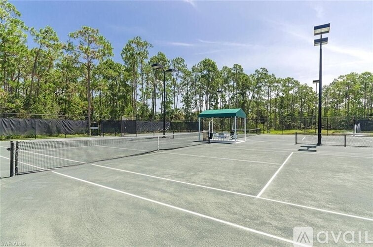 A tennis court with a green roofed shelter and a fence surrounding it.