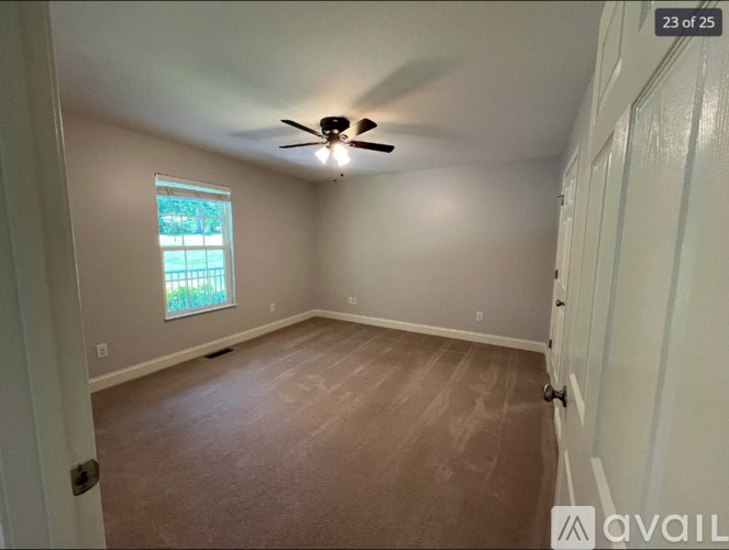 A room with a ceiling fan and a window with a view of trees.