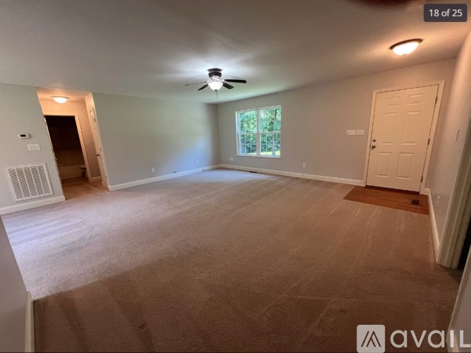 A room with a carpeted floor, a ceiling fan, and a door leading to another room.