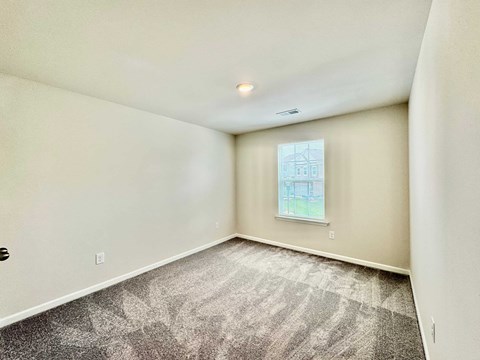 A room with a carpeted floor and a window showing a building outside.