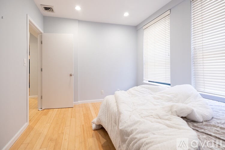 A bedroom with a bed, wooden floor, and a window with blinds.