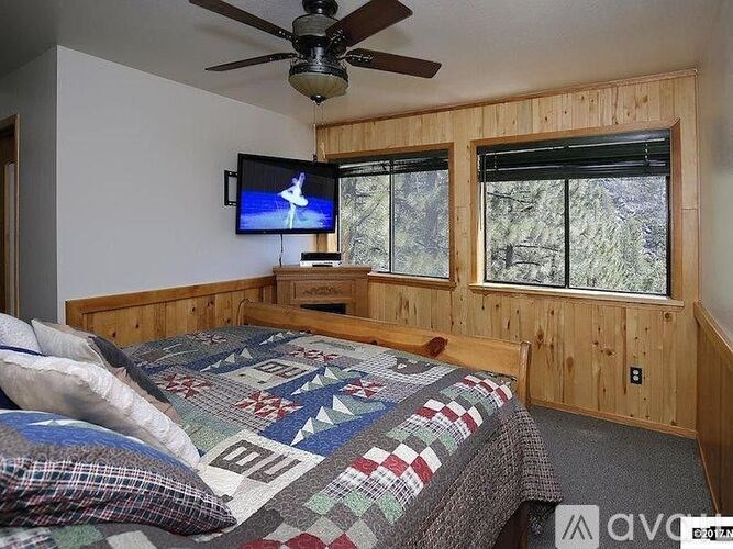 A bedroom with a bed, a ceiling fan, and a window with a view of trees.