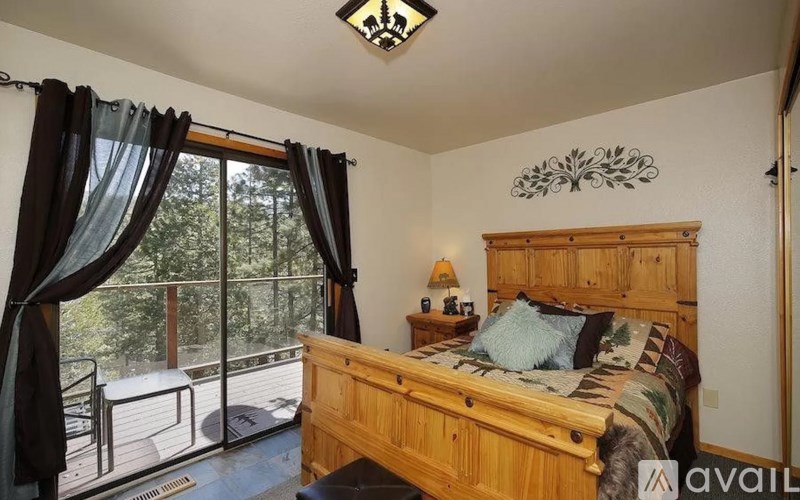 A bedroom with a large bed and a balcony with a view of trees.