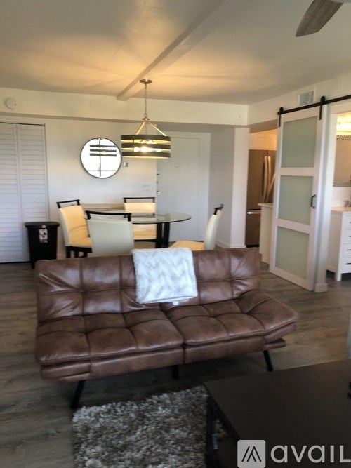 A brown leather couch with a white pillow is in the foreground of a room with a dining table and chairs in the background.