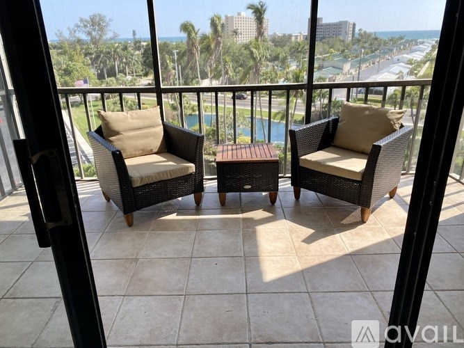 Two chairs and a table are on a balcony overlooking a pool and beach.