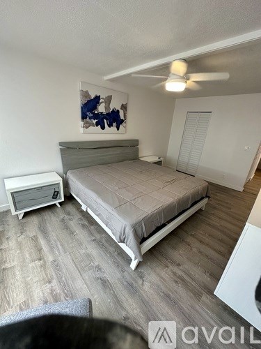 A bedroom with a bed, a ceiling fan, and a painting on the wall.