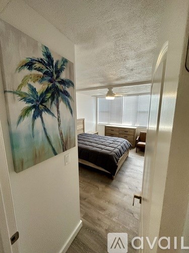 A bedroom with a bed, dresser, and a painting of a palm tree on the wall.