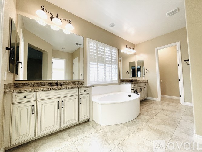 A large, well-lit bathroom with a bathtub, double sinks, and a large mirror.