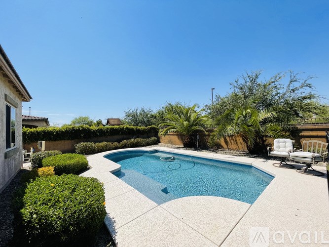 A swimming pool surrounded by a concrete patio and green bushes.