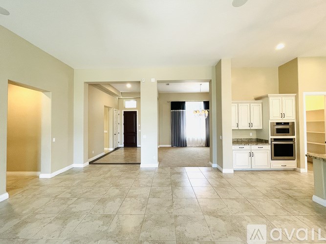 A spacious living room with tiled flooring and a kitchen area with white cabinets and appliances.