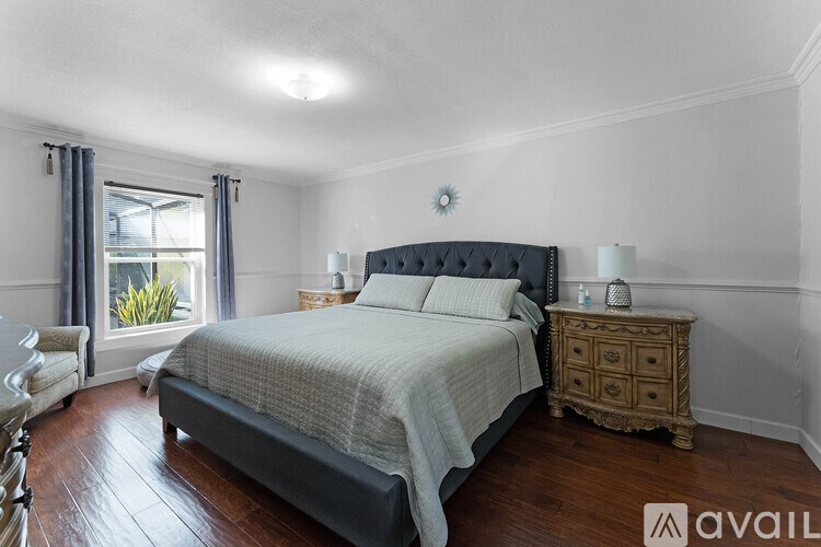 A bedroom with a large bed, a nightstand, and a window with curtains.