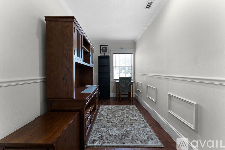 A hallway with a rug on the floor and a wooden cabinet on the left.
