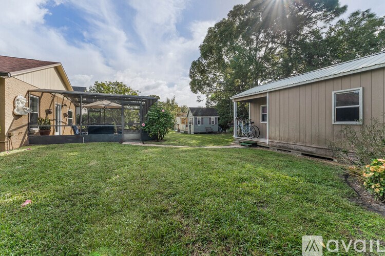 A sunny day in a backyard with a house, a shed, and a lawn.