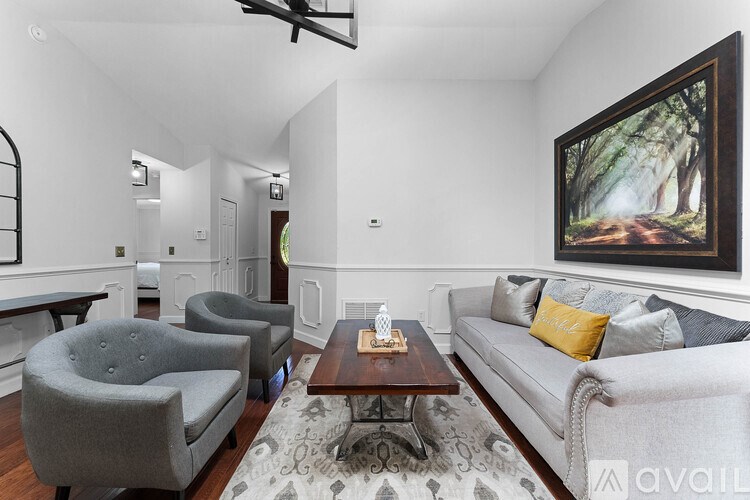 A living room with a grey couch, a grey armchair, a coffee table, and a painting on the wall.