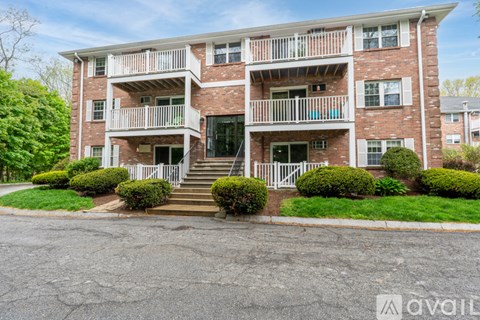 A brick apartment building with a white balcony and stairs leading to the front door.