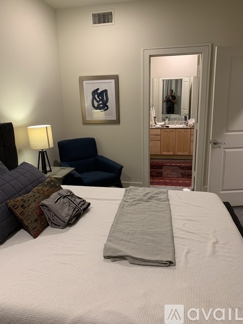 A bedroom with a bed, a chair, a lamp, and a framed picture on the wall.