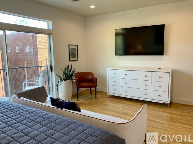 A bedroom with a bed, a chair, a plant, and a TV mounted on the wall.