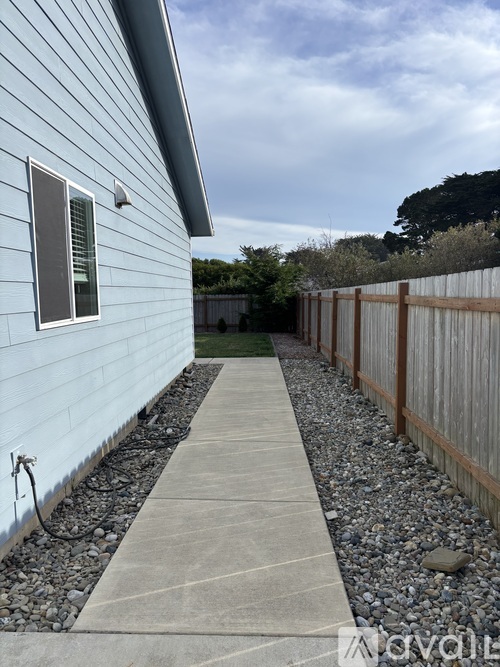 A concrete walkway leads to a blue house with a wooden fence on one side.