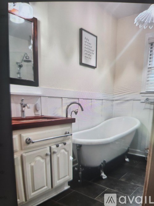 A white claw foot tub sits in a bathroom with a wooden vanity and a mirror.