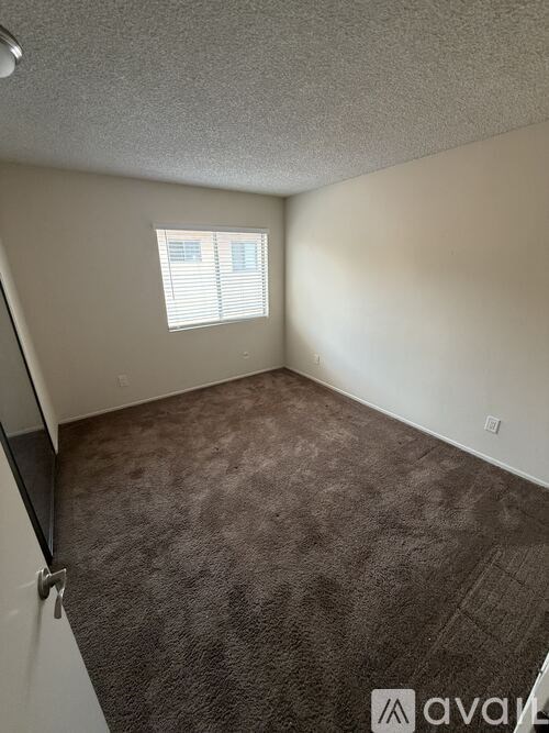 A room with a carpeted floor and a window with blinds.
