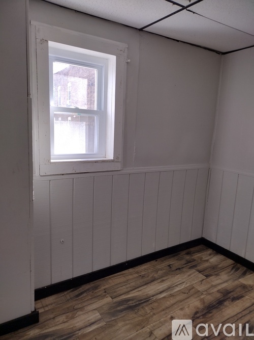 A bed with a grey blanket and a white pillow is in a room with white walls.