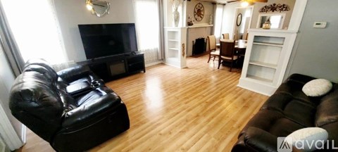 A living room with a black leather couch and a wooden floor.