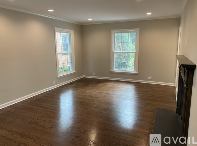 A spacious room with wood flooring and two windows.