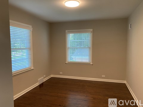 A room with wooden floors and two windows with blinds.
