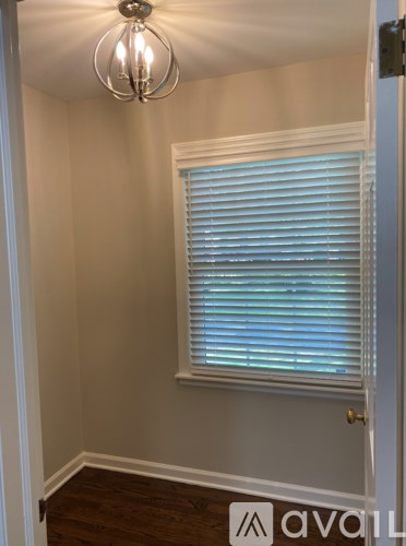 A room with a window covered by white blinds and a chandelier hanging from the ceiling.