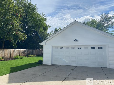 A white garage with a wooden fence and trees in the background.