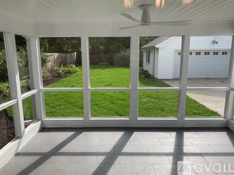 A white patio with a ceiling fan and a view of a white house and green lawn.
