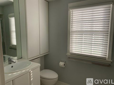 A bathroom with a toilet, sink, and window with blinds.