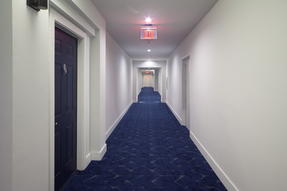 a corridor with a blue carpet and a red exit sign at the end of it