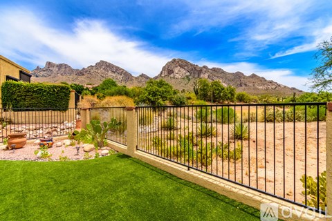 A backyard with a fence, green grass, and mountains in the background.