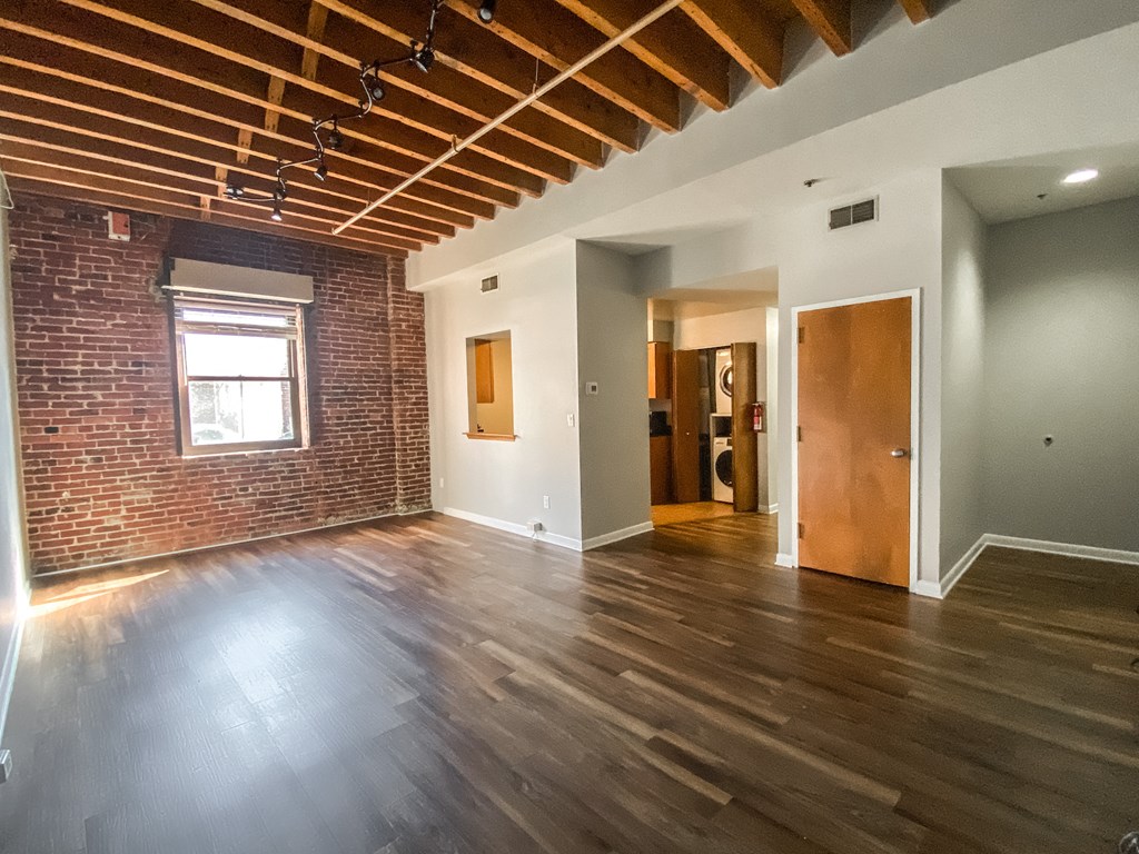 an empty living room with a brick wall and wooden floors