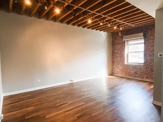 an empty living room with wood floors and a brick wall