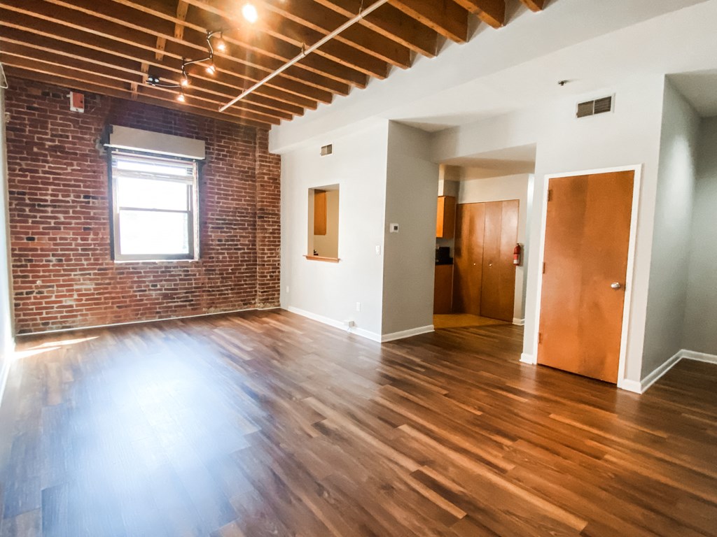 an empty living room with wood floors and a brick wall