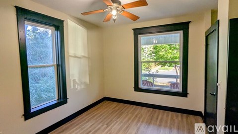 A room with a ceiling fan and two windows.