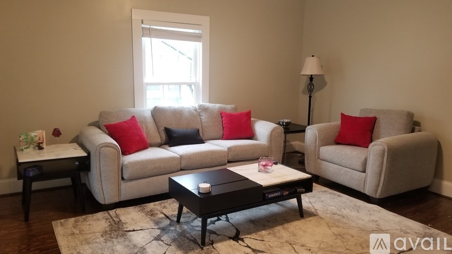 A living room with a grey couch, red pillows, a black coffee table, and a lamp.