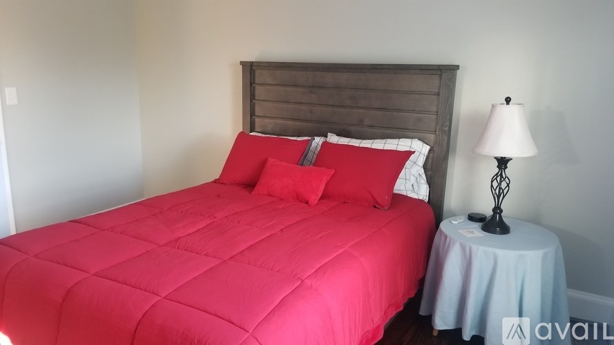 A bed with a red comforter and two red pillows sits next to a lamp on a small table.