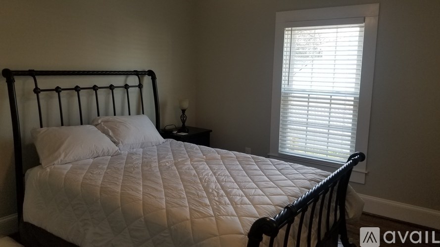 A bed with a white comforter and two pillows sits in a room with a window.