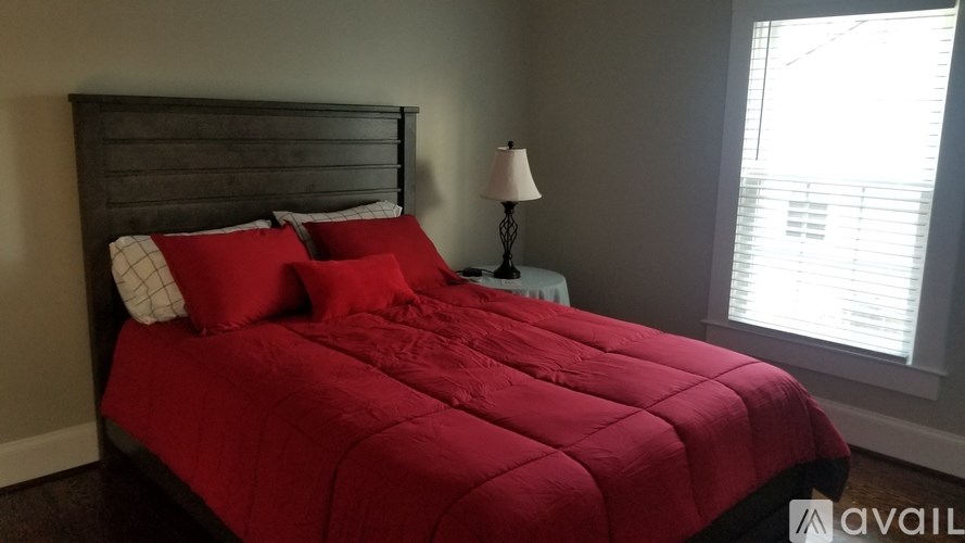 A bed with a red comforter and pillows with a lamp on a nightstand.
