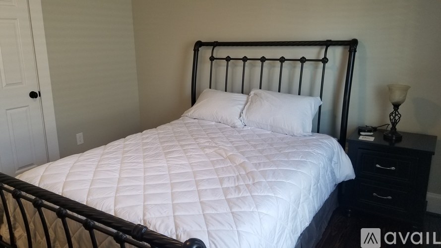 A bed with a white comforter and two pillows sits in a room with a black metal headboard.