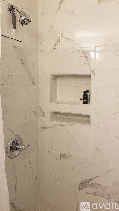 A shower area with a marble wall and a rectangular shelf.