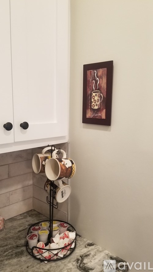 A painting hangs on the wall above a shelf with mugs on it.