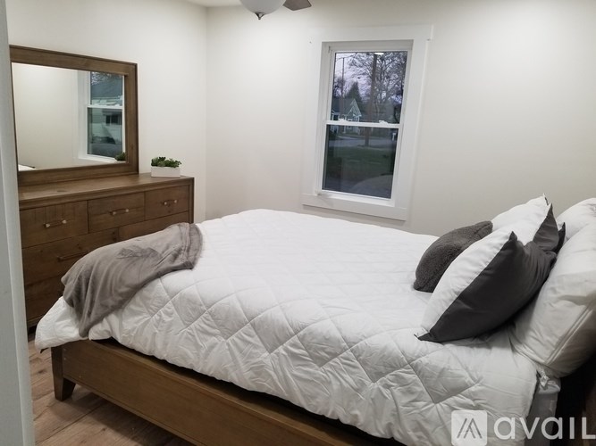 A bedroom with a bed, dresser, mirror, and window.